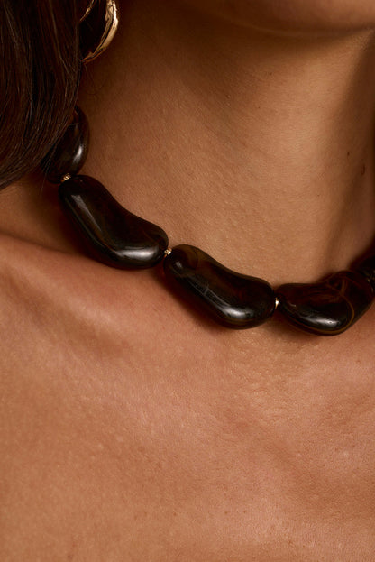 Chunky dark stone choker with glossy organic beads worn close around the neck.