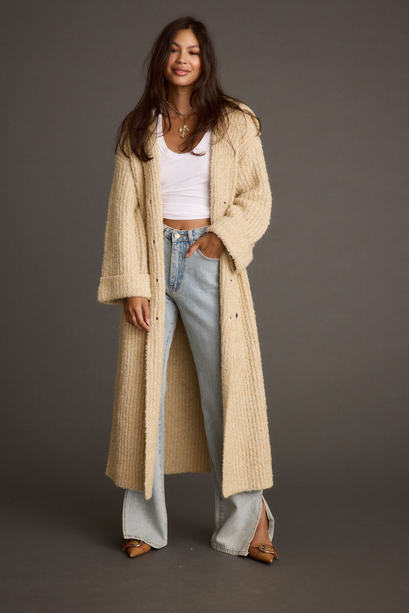 Cream knit long cardigan coat worn open over a white tee and jeans.