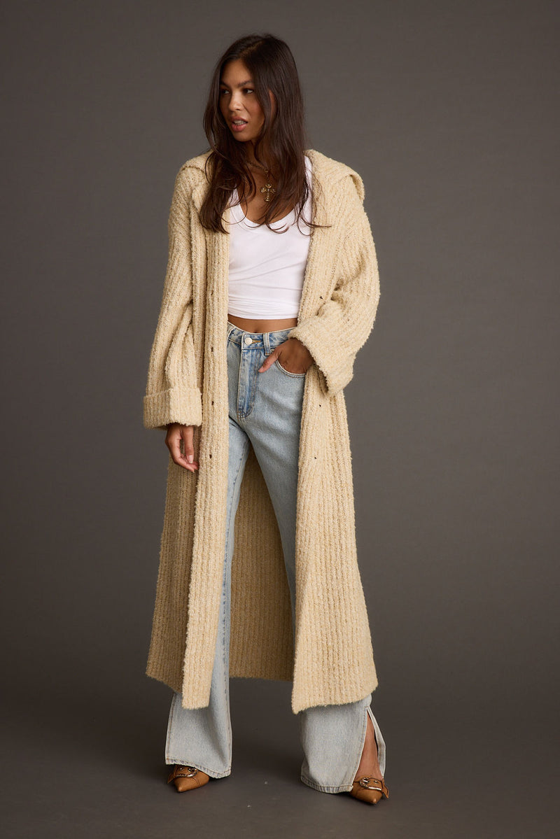 Cream knit long cardigan coat worn open over a white tee and jeans.