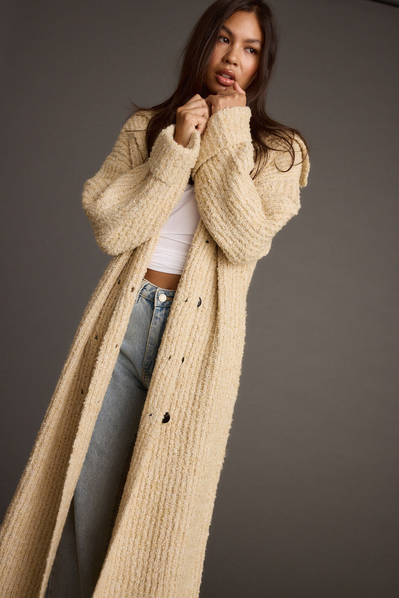 Model wears cream knit long cardigan coat open over white tee and jeans.