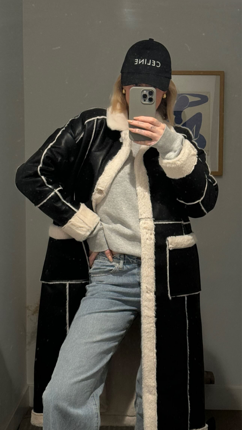 Black faux leather long coat with cream sherpa trim styled over jeans in a mirror selfie.
