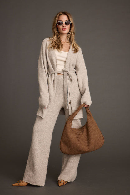 Model wears oatmeal knit sweater pants with matching belted cardigan and woven brown bag.