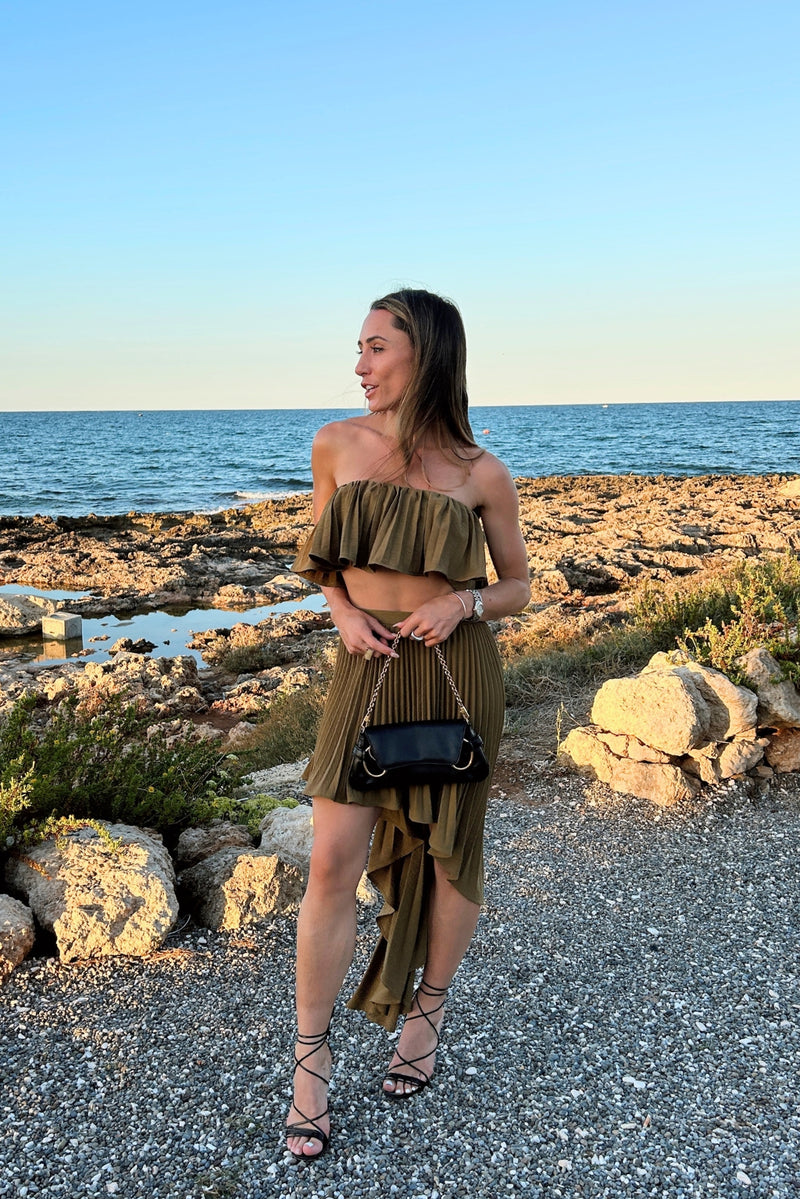 Pleated olive asymmetrical midi skirt with matching ruffle crop top on a rocky coastline.