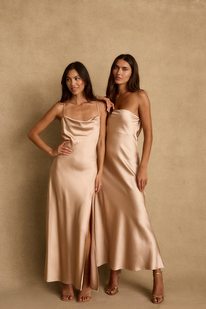 Two people in champagne satin maxi dresses, one strapless with side slit, against tan backdrop.