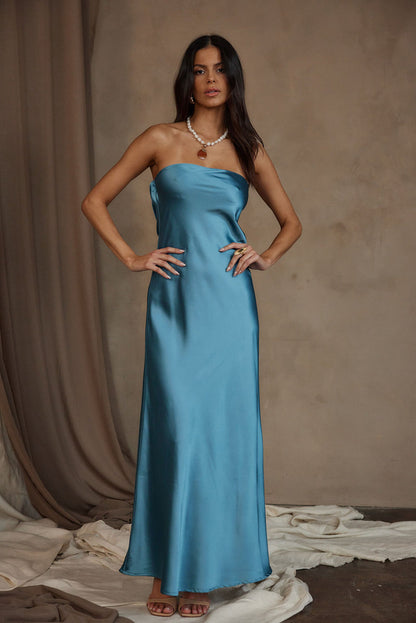 Blue satin strapless maxi dress with pearl necklace, modeled against draped neutral backdrop.