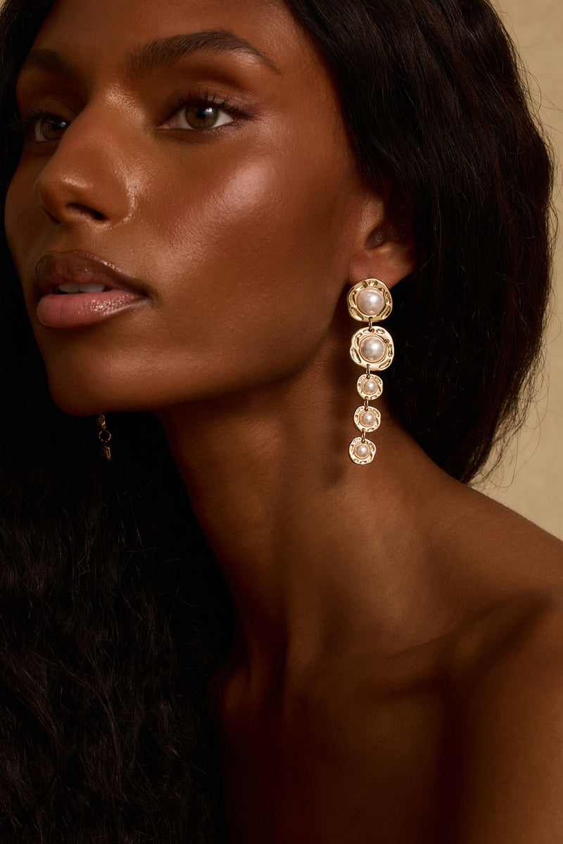 Model wearing the 12th Tribe Olivia Gold and Pearl Earrings, elegant gold and pearl drop earrings featuring a multi-pendant design with delicate pearl accents and a push back closure. Perfect for elevating your vacation maxi dress look, summer soirées, and nights out on the town.