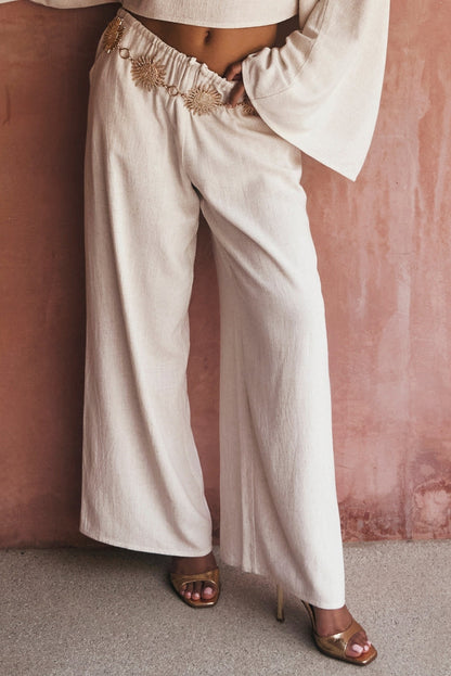 Wide-leg white linen pants styled with a gold sun belt and metallic heels.