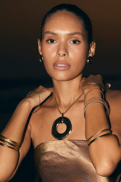 Gold circular pendant necklace with stacked bangles and a metallic dress, resort evening attire for women.
