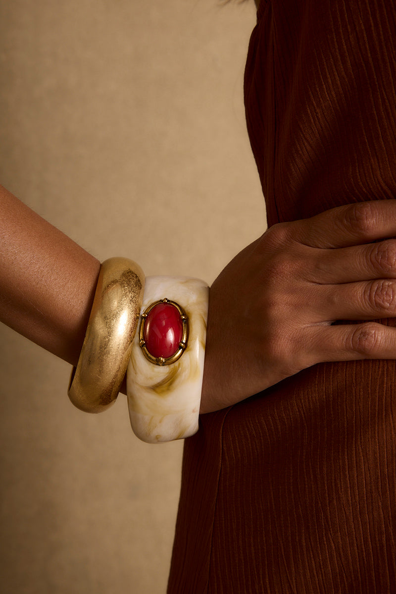 Solstice bangle set: brushed gold cuff and cream marbled bangle with red stone, worn on wrist.