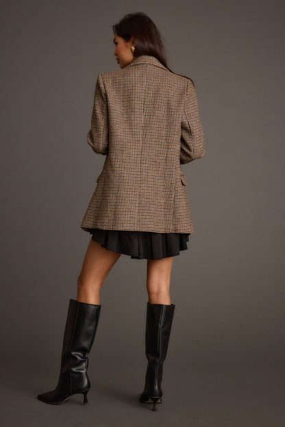 Back view of brown houndstooth plaid blazer styled with black mini skirt and knee boots.