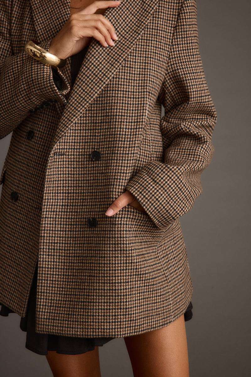 Detail of brown houndstooth plaid blazer with double-breasted black buttons and gold cuff bracelet.