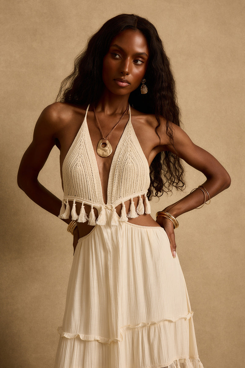Cream crochet halter maxi dress with tassel fringe trim and waist cutouts on a model.