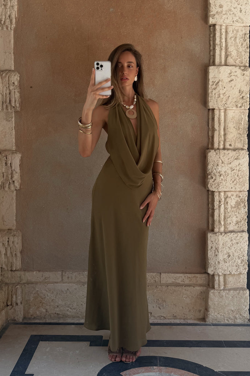 Model wearing the 12th Tribe Zela Olive Cowl Maxi Dress, a vacay-ready flowy satin maxi dress featuring a dramatic front cowl, deep low back, and halter silhouette. Perfect for maxi dresses for beach vacations, Caribbean vacation looks, and warm summer nights out on the town.