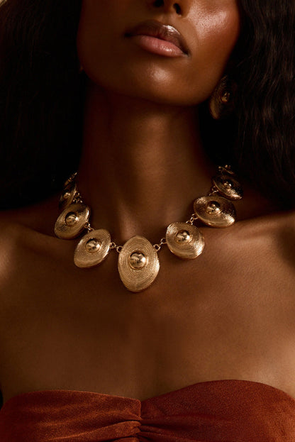Gold statement necklace with textured domed discs worn on-model with matching gold earrings.